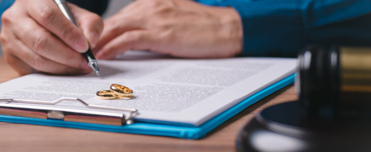 A man is writing on a piece of paper with a pen. The paper has a ring on it